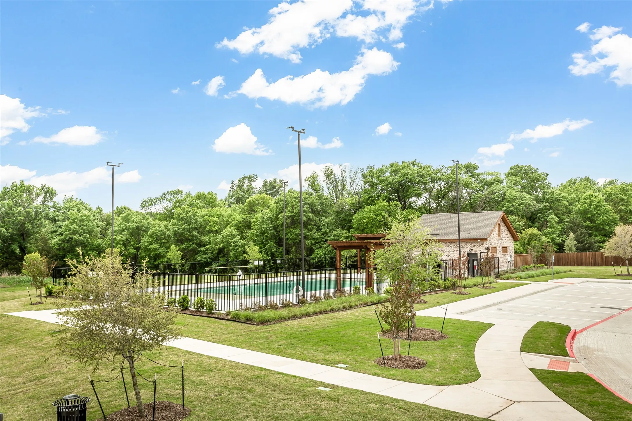 Community swimming pool with a surrounding black metal fence, accompanied by a stone-clad building with a shingled roof