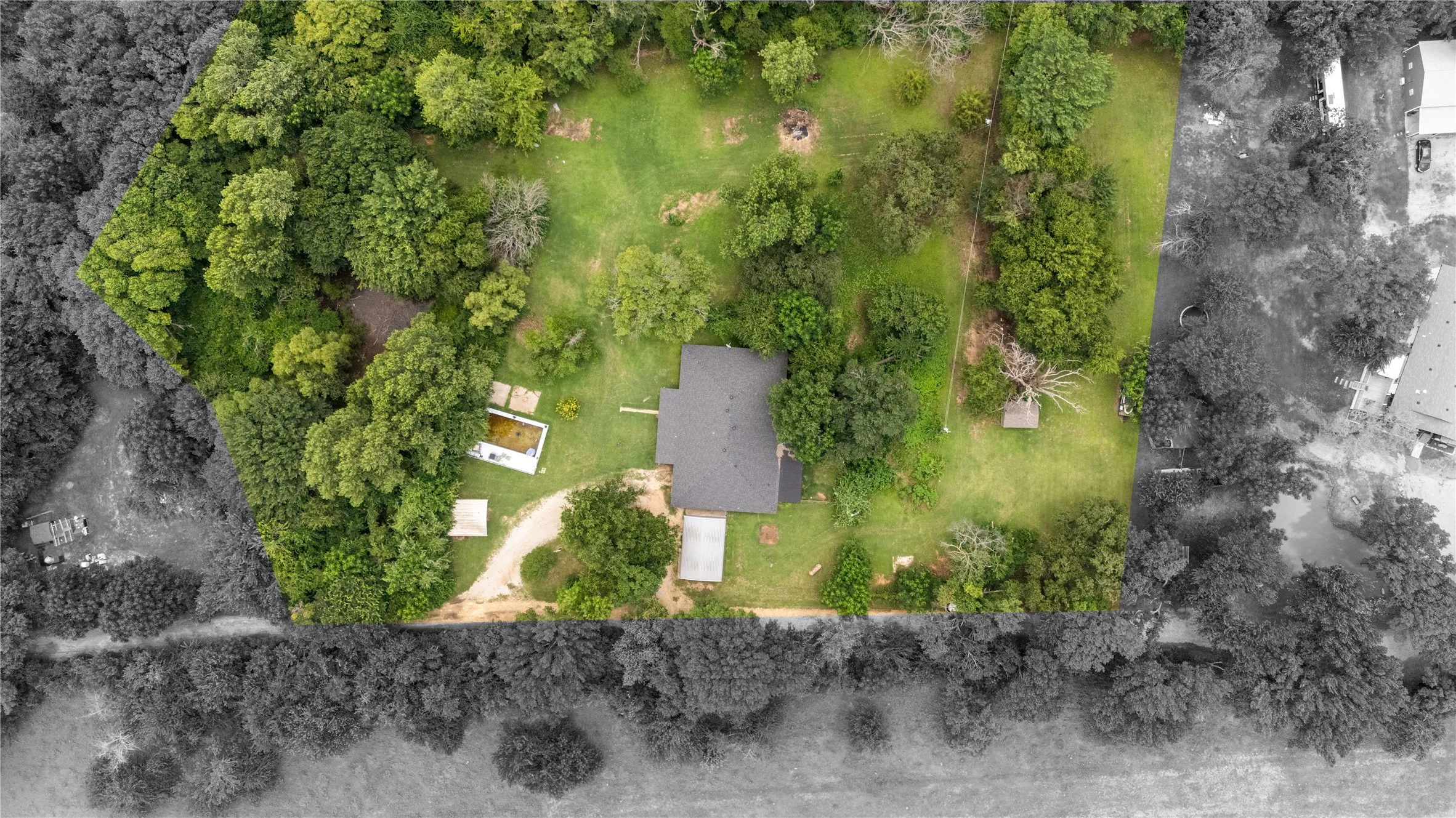Expansive property featuring a central residence with a dark roof and a surrounding landscape of mature trees and green space