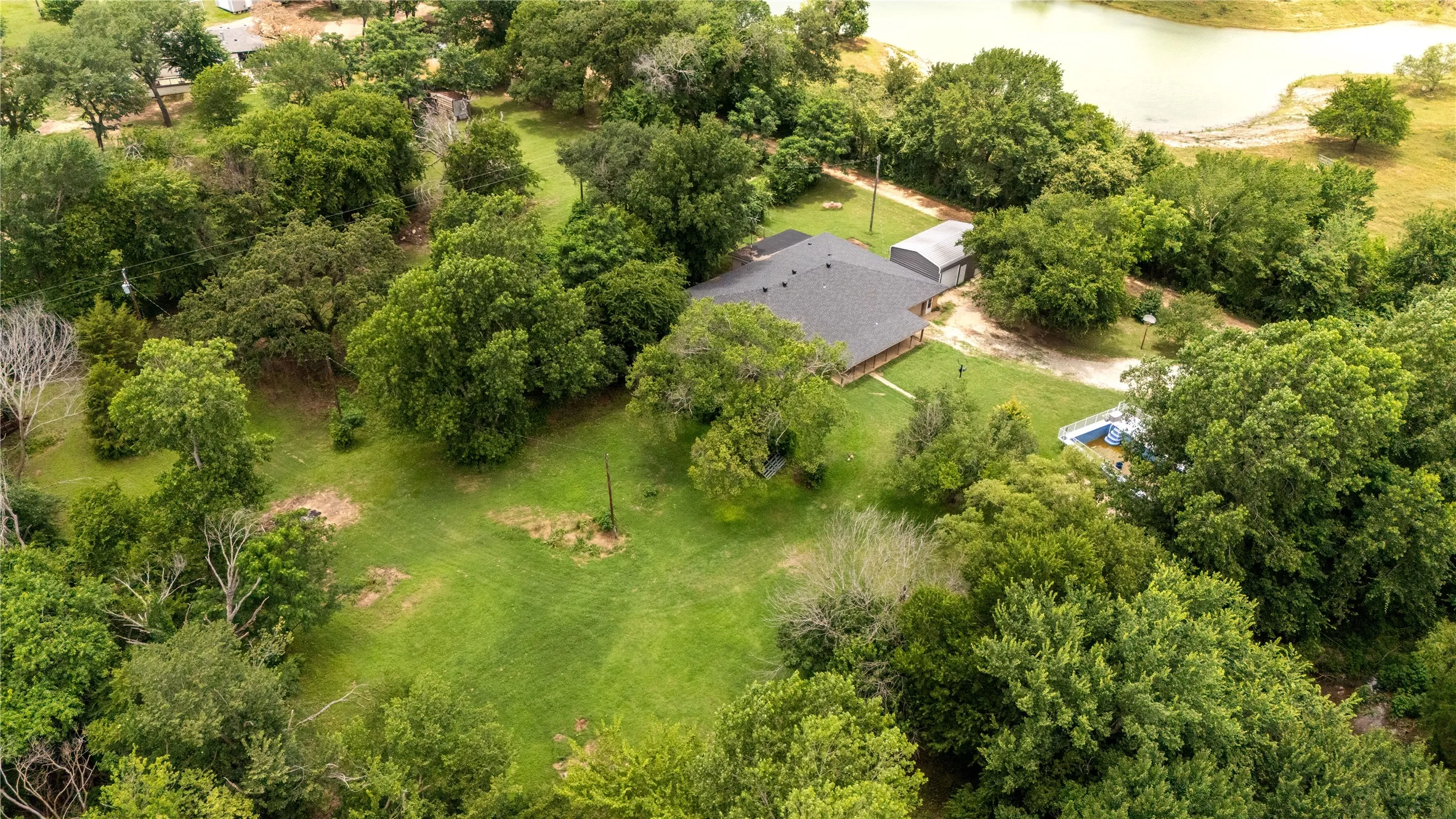 Expansive property featuring a single-story residence with a dark shingle roof, a detached metal structure, and a partially visible pool