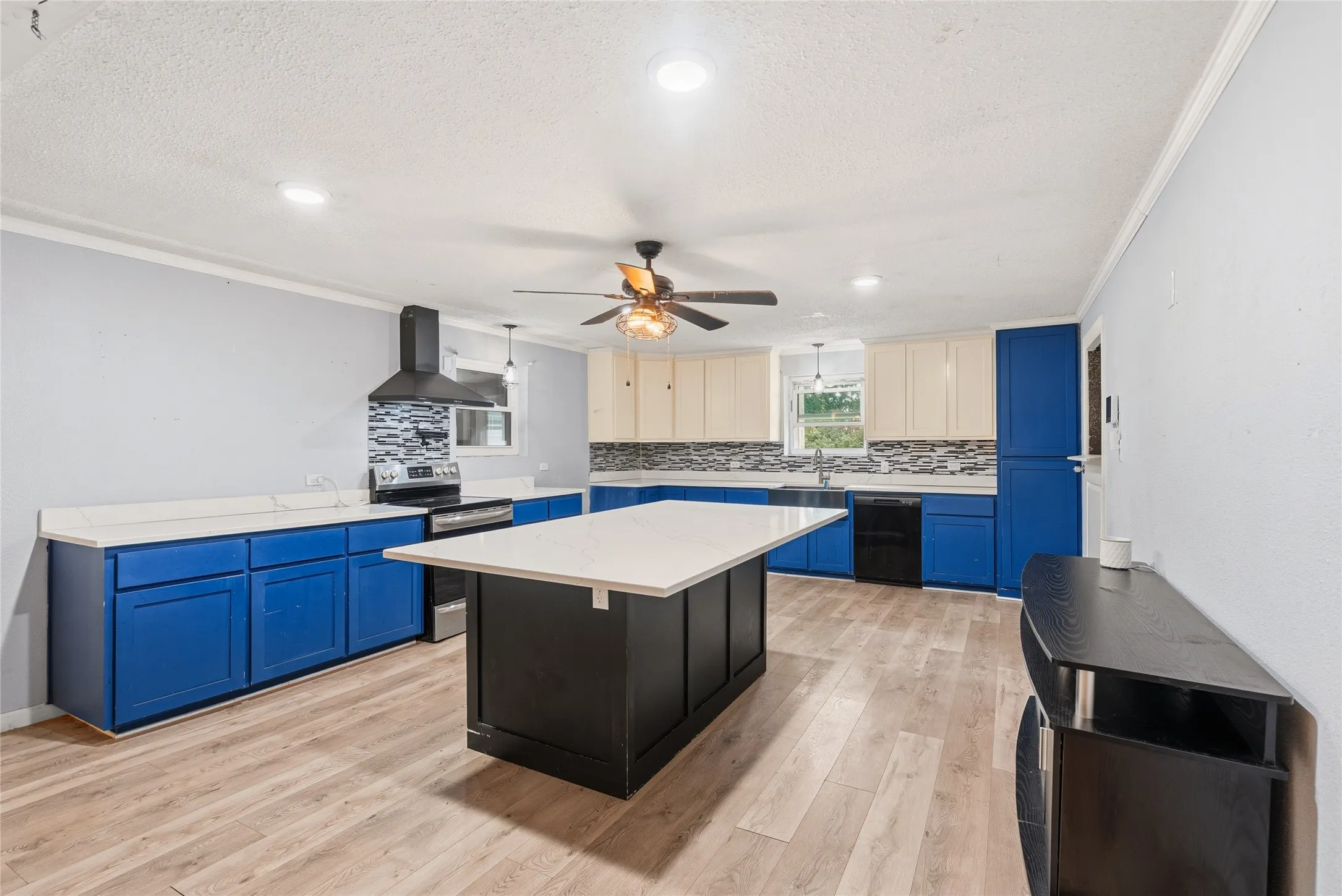 Kitchen featuring a central island with a solid surface countertop, blue and cream cabinetry, patterned tile backsplash, stainless steel range with range hood, and wood-finish flooring