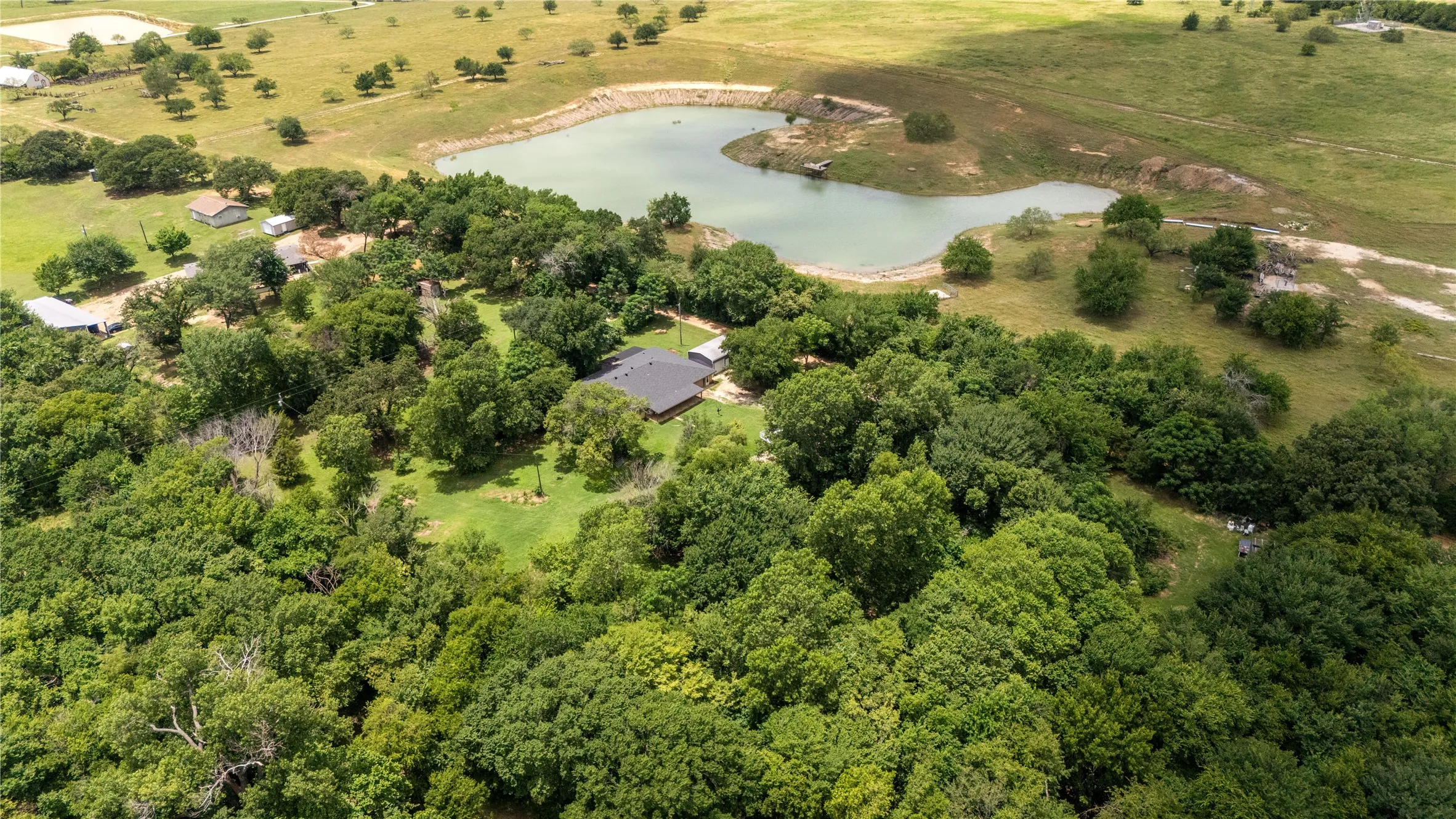 Expansive aerial perspective showcasing a property surrounded by mature trees, featuring a distinct body of water