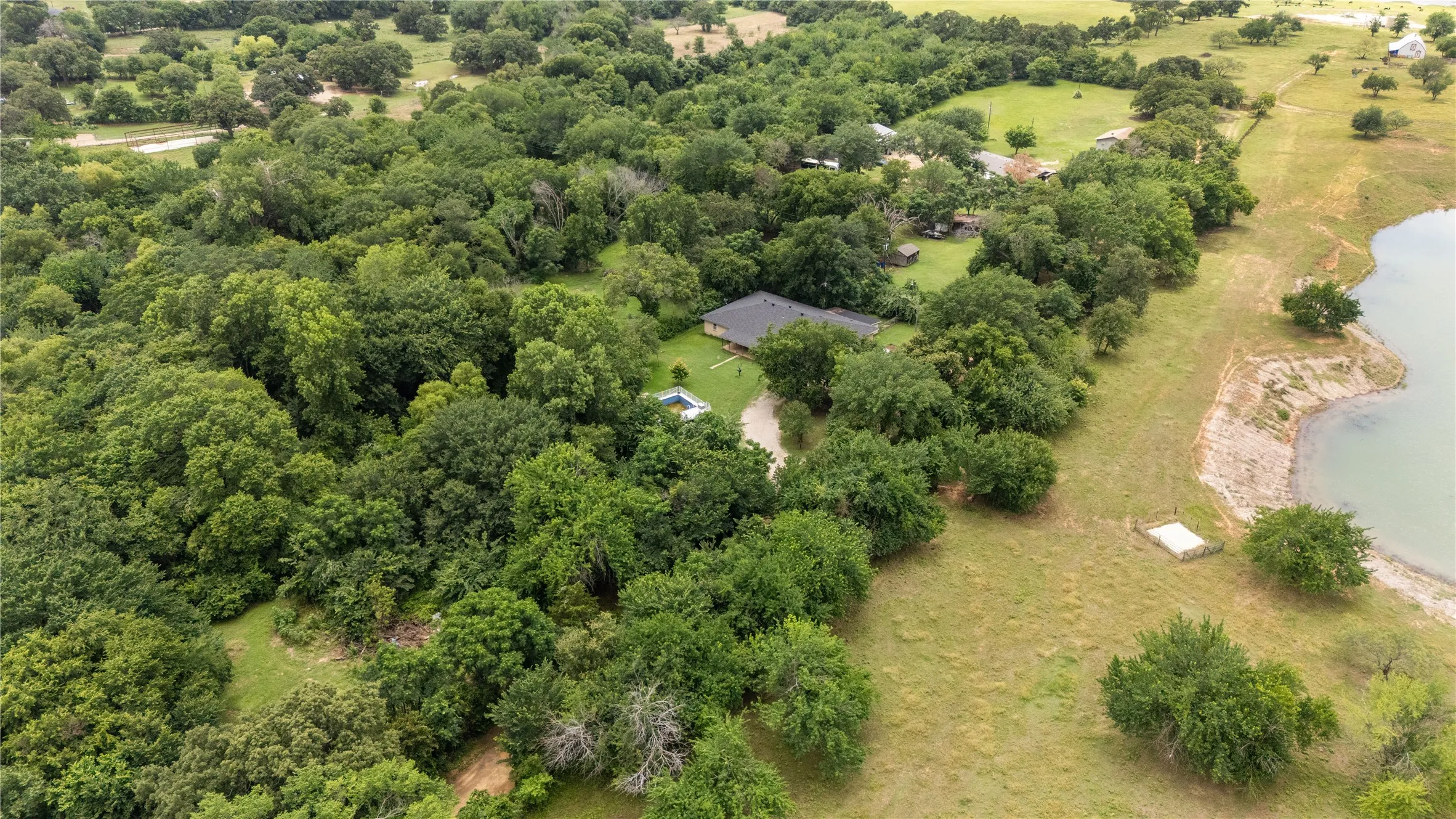 Expansive acreage featuring abundant mature trees, a private residence with a dark roof, a swimming pool, and natural water frontage