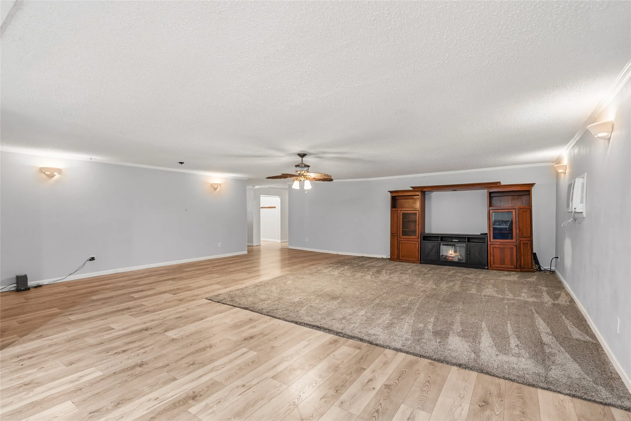 Spacious living area featuring wood-finish flooring, a built-in media center with an electric fireplace, a ceiling fan, and wall sconces