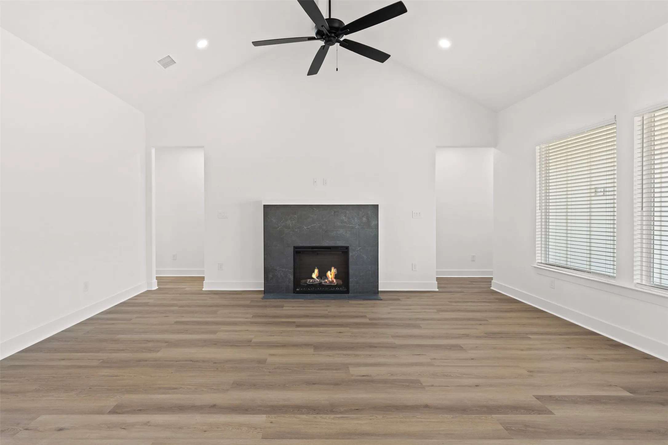 Spacious room featuring vaulted ceilings, wood-finish flooring, and a modern fireplace with a dark stone-look surround