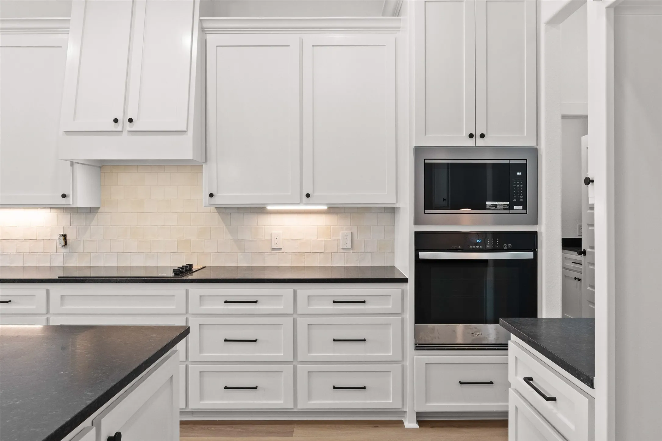 Contemporary kitchen featuring white shaker cabinetry, dark countertops, a built-in microwave, a wall oven, and a tiled backsplash