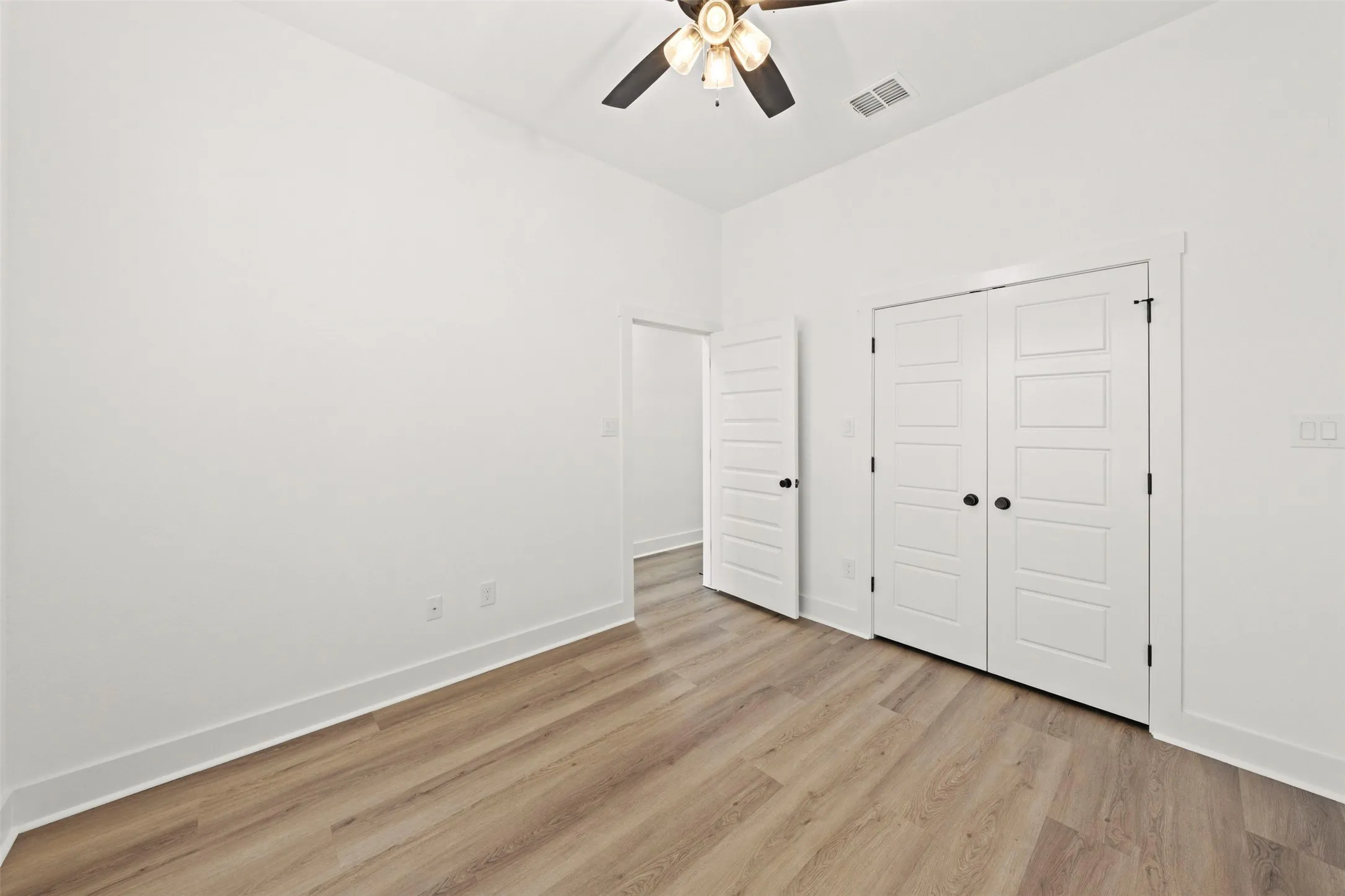 Bright room featuring wood-finish flooring, white baseboards, a ceiling fan with light fixture, and a double-door closet with black hardware