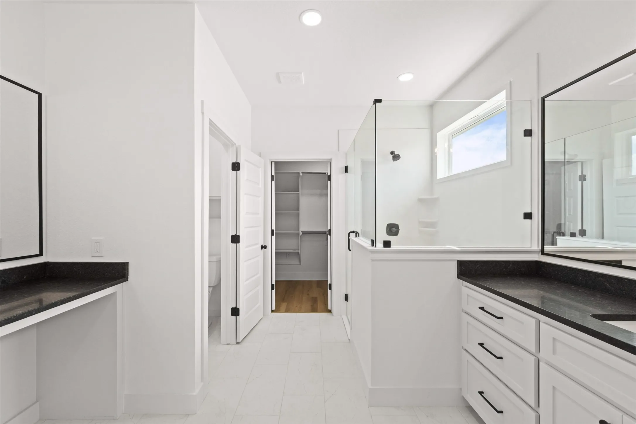 Contemporary bathroom featuring dual vanities with dark countertops, a glass-enclosed shower, a privacy window, and tile flooring