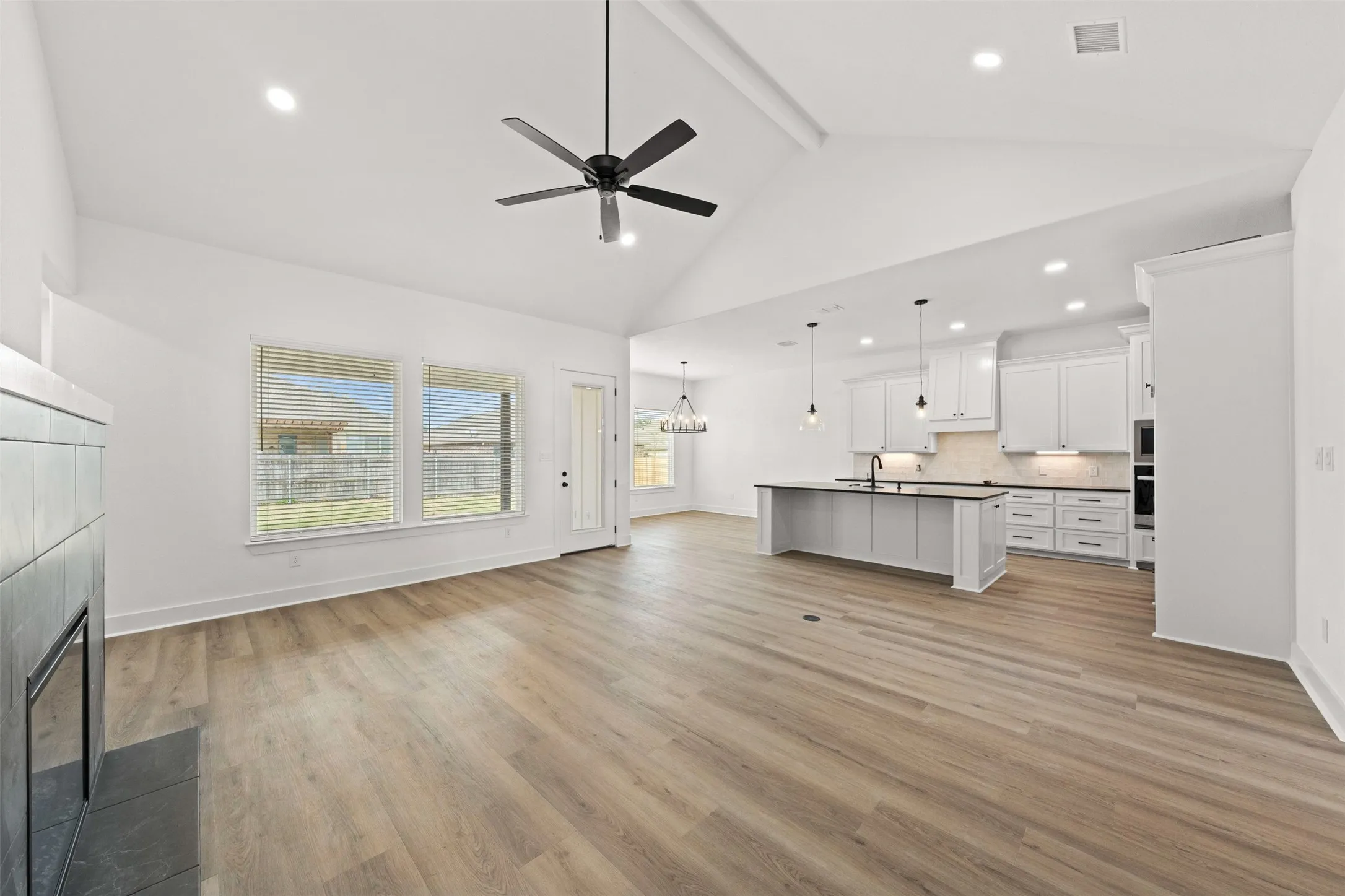 Open-concept living space featuring vaulted ceilings, wood-finish flooring, a modern fireplace, recessed lighting, and a kitchen with white cabinetry and a central island