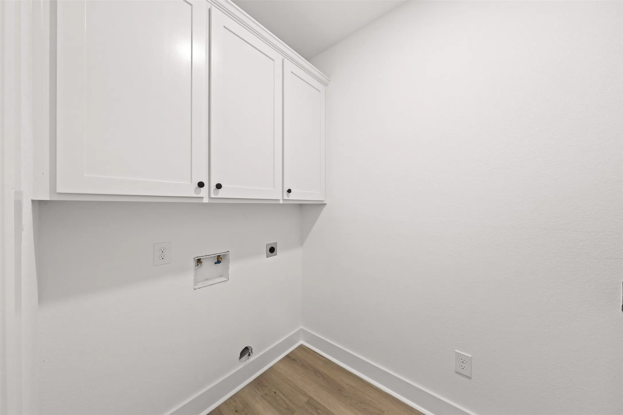 White shaker cabinetry with crown molding and matte black hardware, wood-finish flooring, and white baseboards
