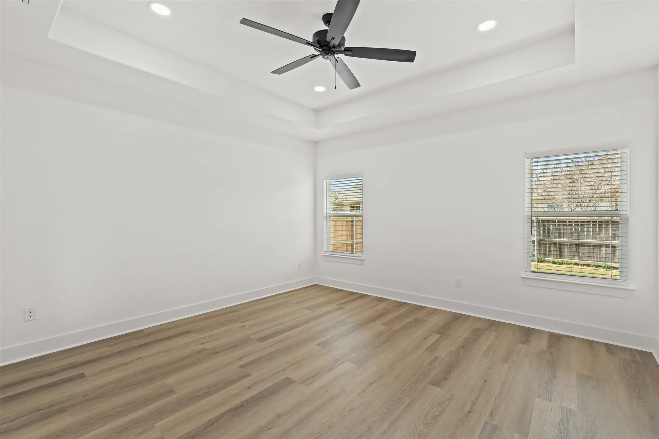 Spacious room with a tray ceiling, recessed lighting, and a matte black ceiling fan