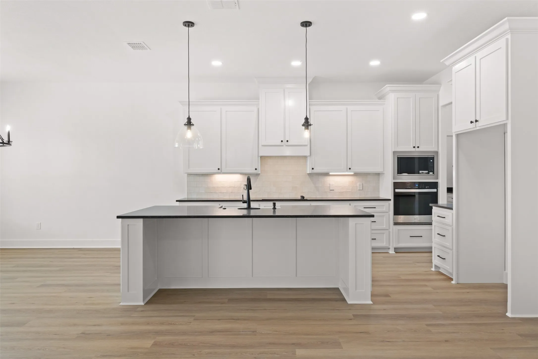 Bright kitchen featuring a central island with a sink, white cabinetry, dark countertops, and integrated stainless steel appliances