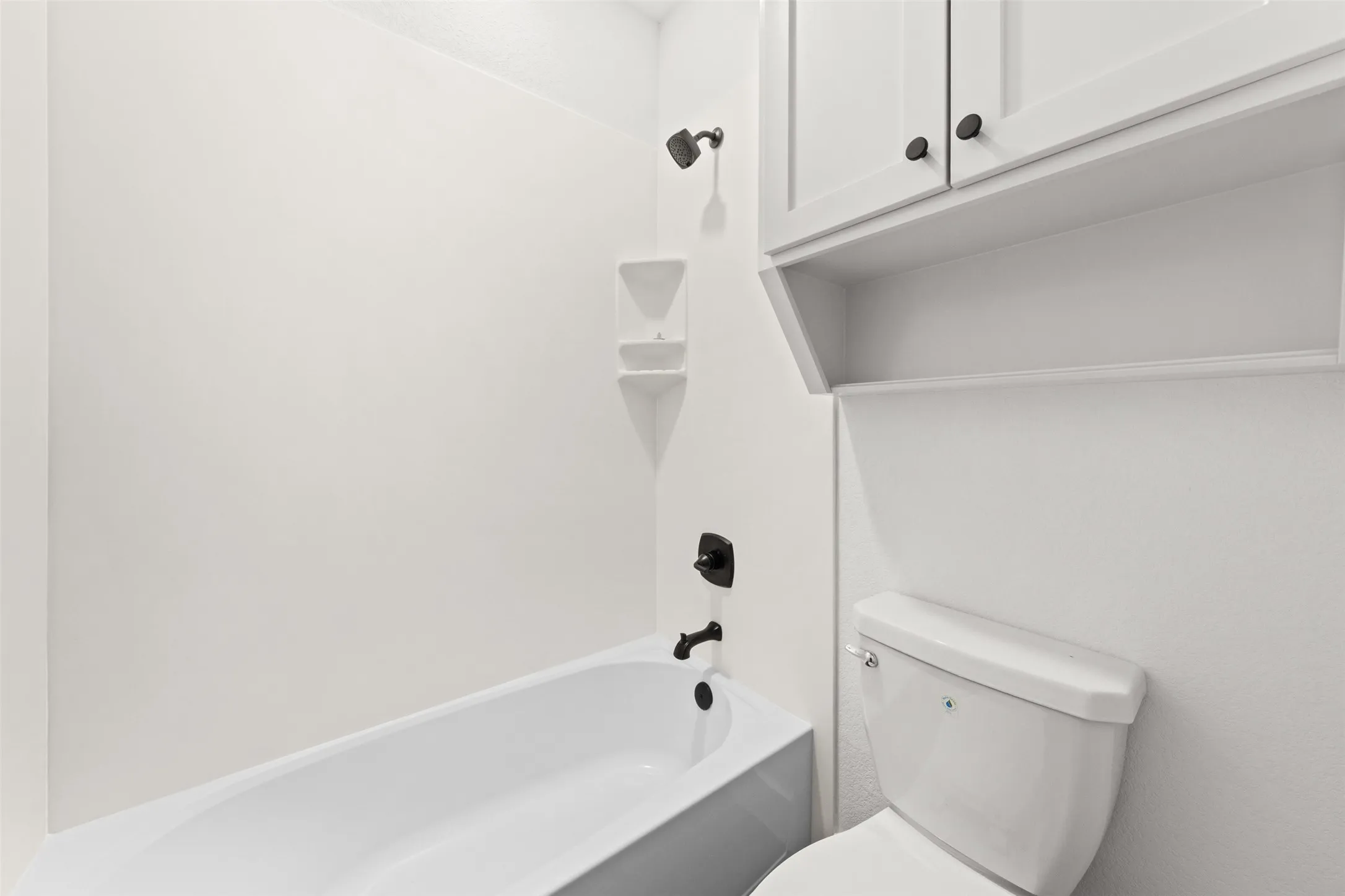 White bathtub with black fixtures, integrated corner shelving, and an overhead showerhead