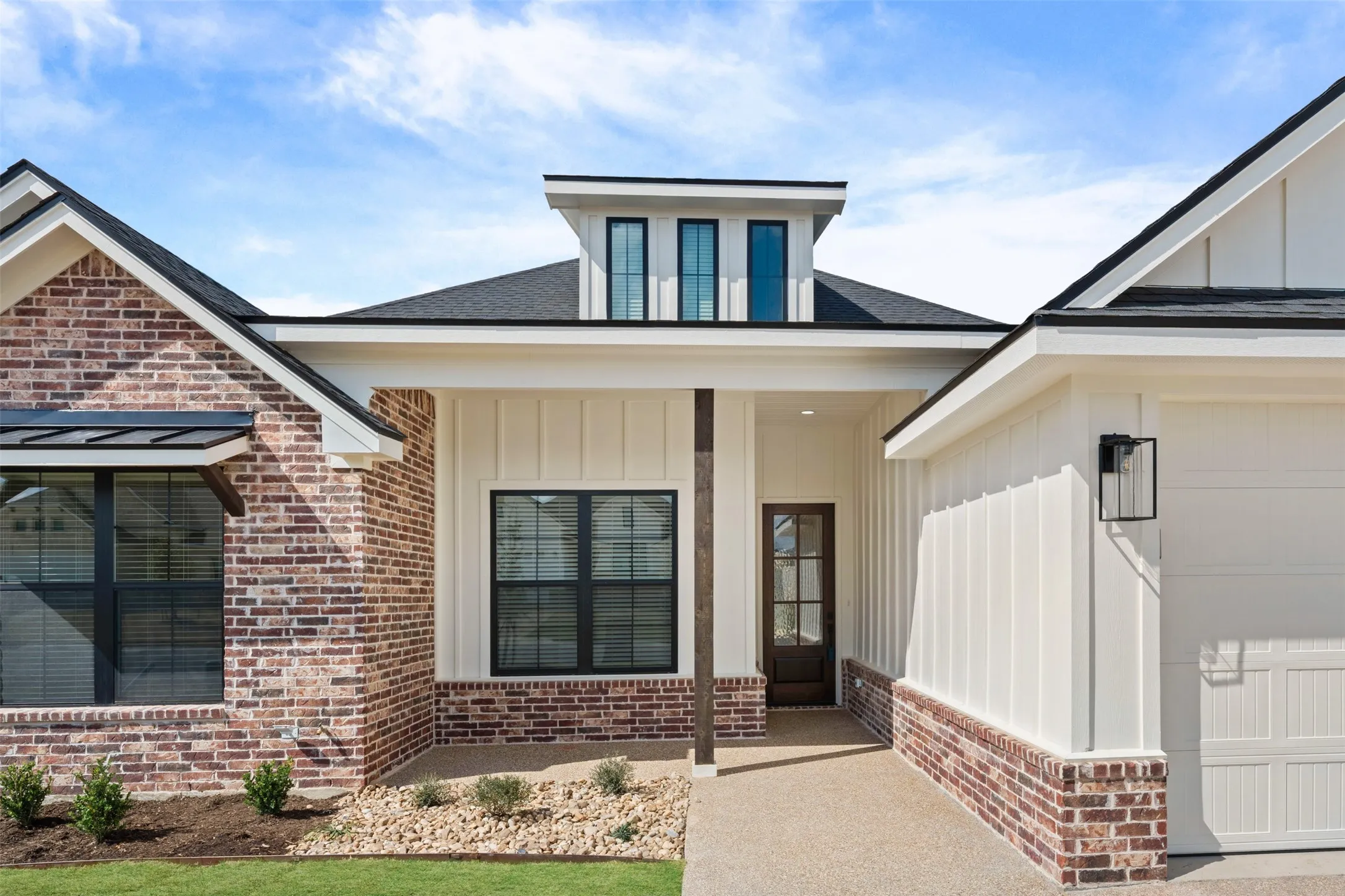 Modern farmhouse exterior featuring a prominent gabled roofline, brick and vertical board-and-batten siding, black-framed windows, and a covered entry with a dark wood-paneled door