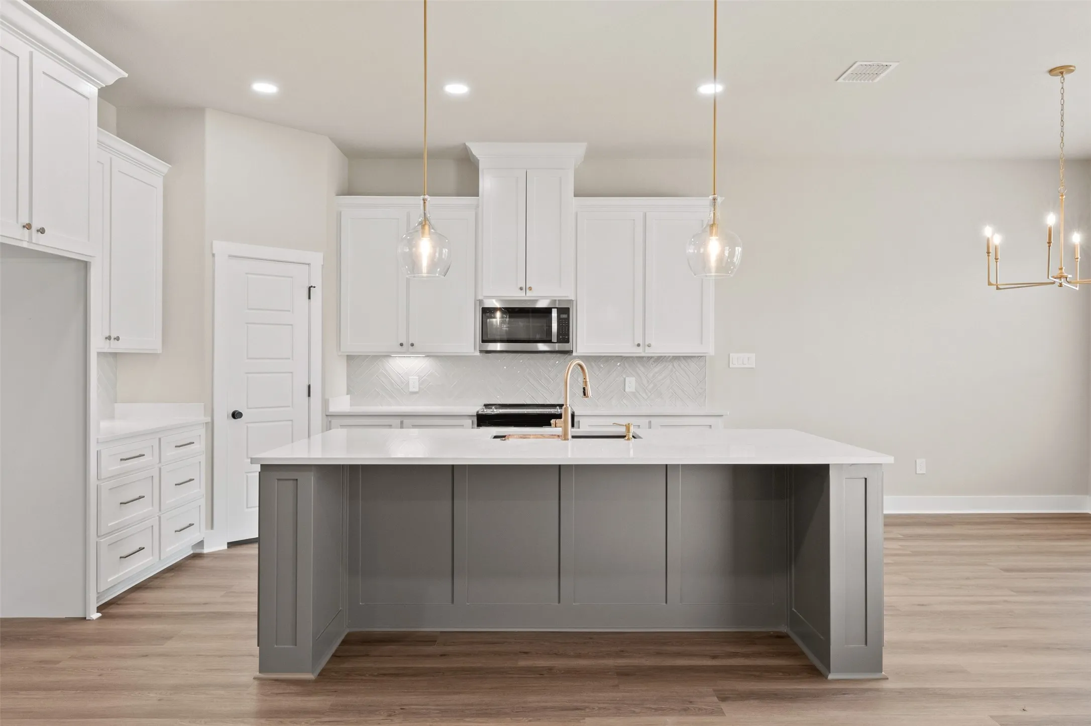 Modern kitchen featuring a spacious gray island with a white countertop, white cabinetry, brass pendant lighting, and wood-finish flooring