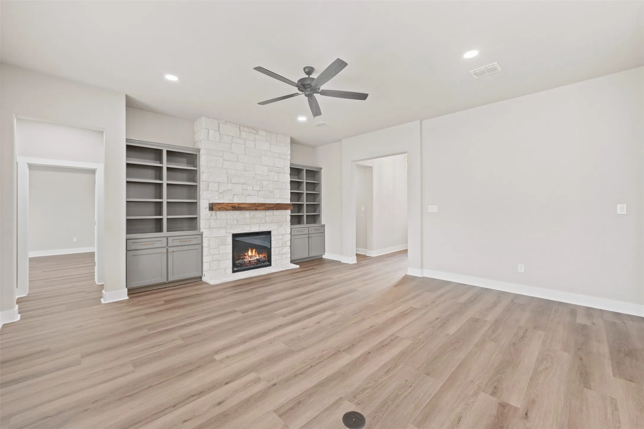 Spacious room featuring wood-finish flooring, a stone-clad fireplace with a wood mantel, and built-in shelving with lower cabinetry