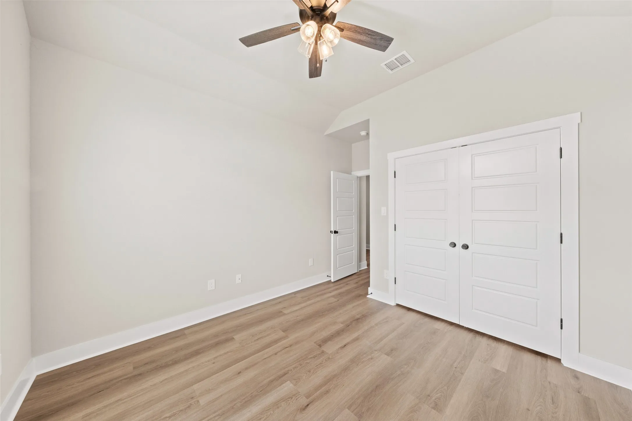 Spacious room featuring wood-finish flooring, white baseboards, and a modern ceiling fan with integrated lighting