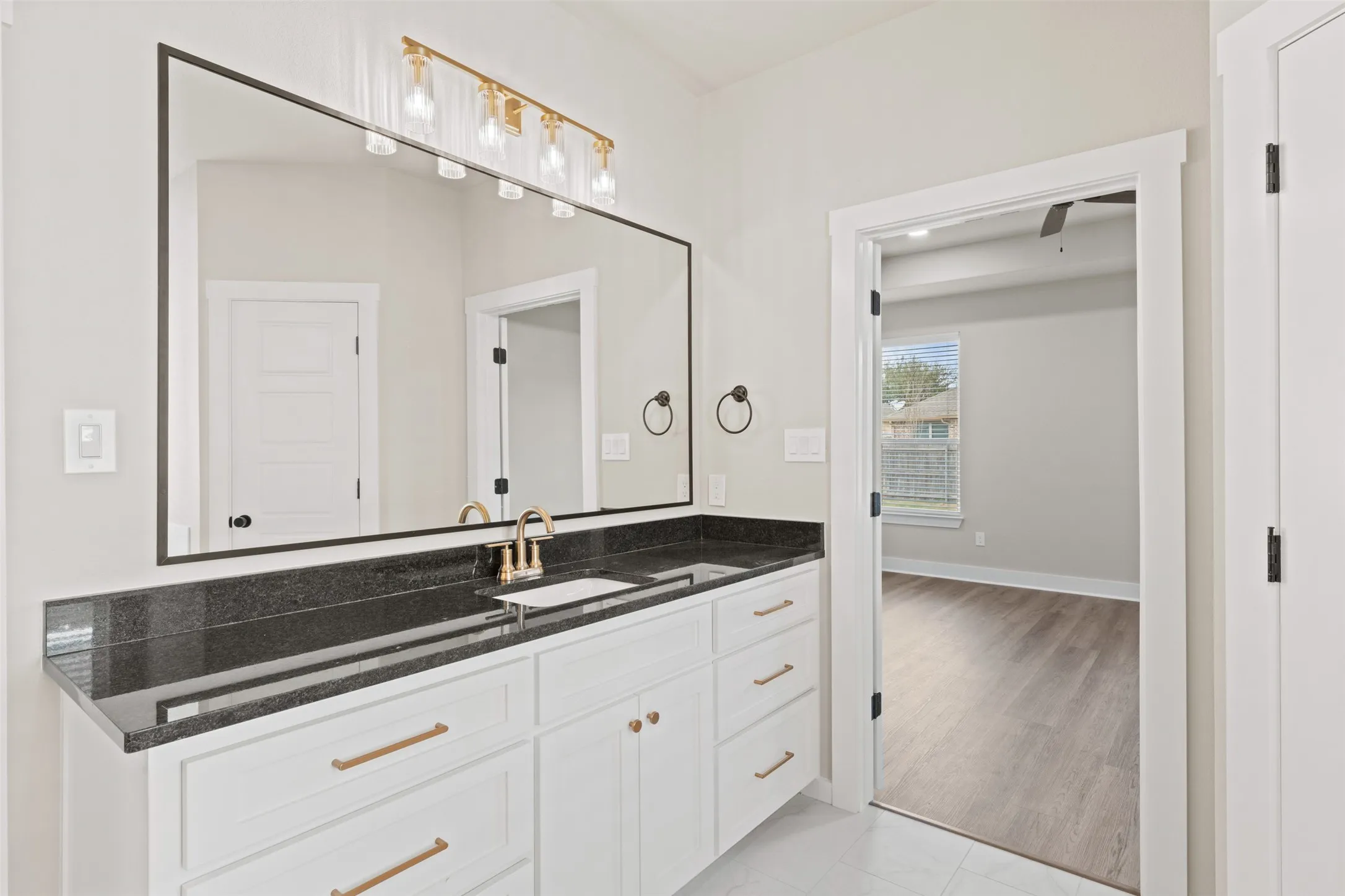 Bathroom vanity featuring a large mirror with a black frame, a dark stone countertop, and a white cabinet with gold-toned hardware
