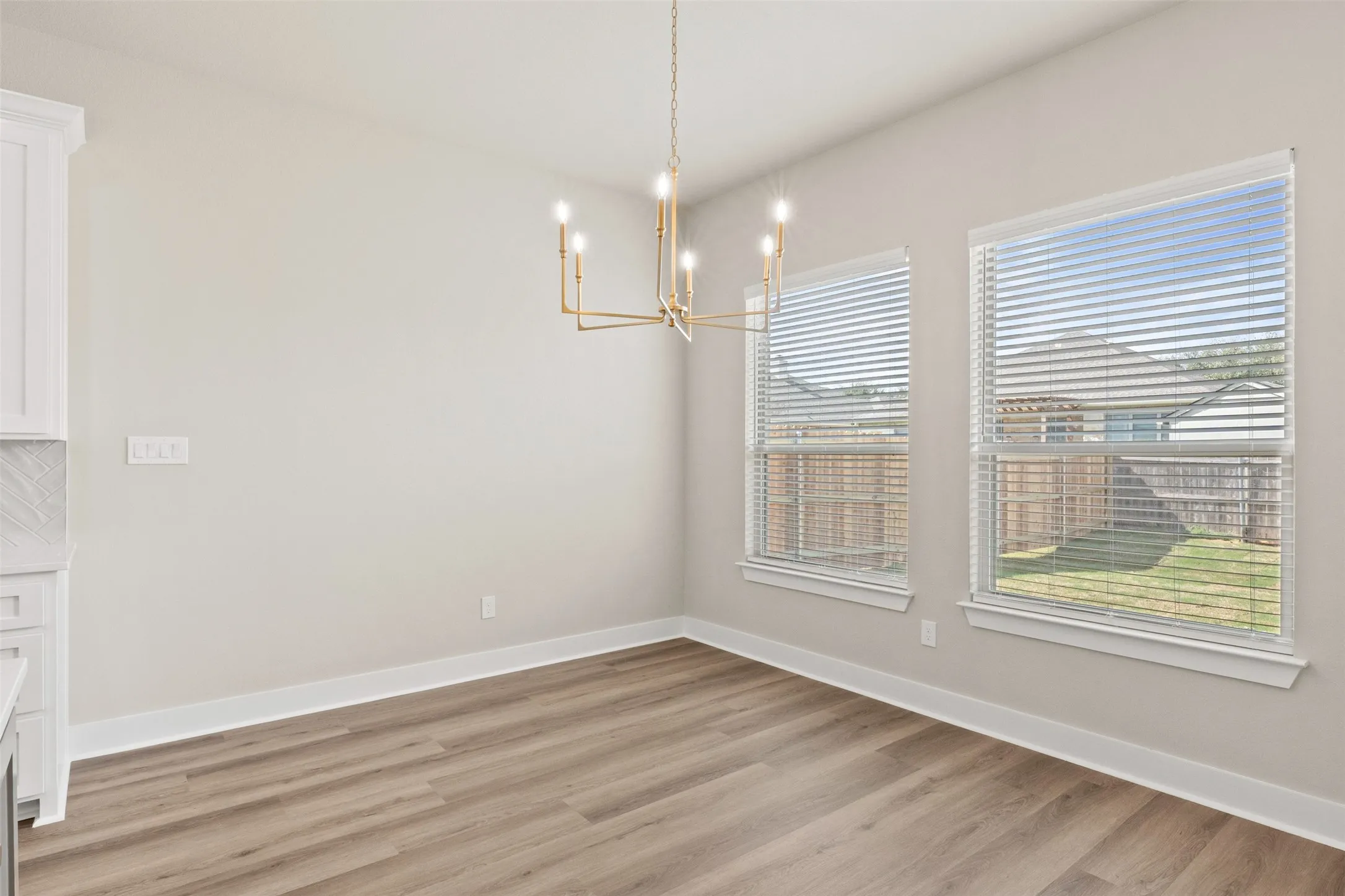 Dining area featuring wood-finish flooring, a modern gold-tone chandelier, two windows with blinds, and light-toned walls