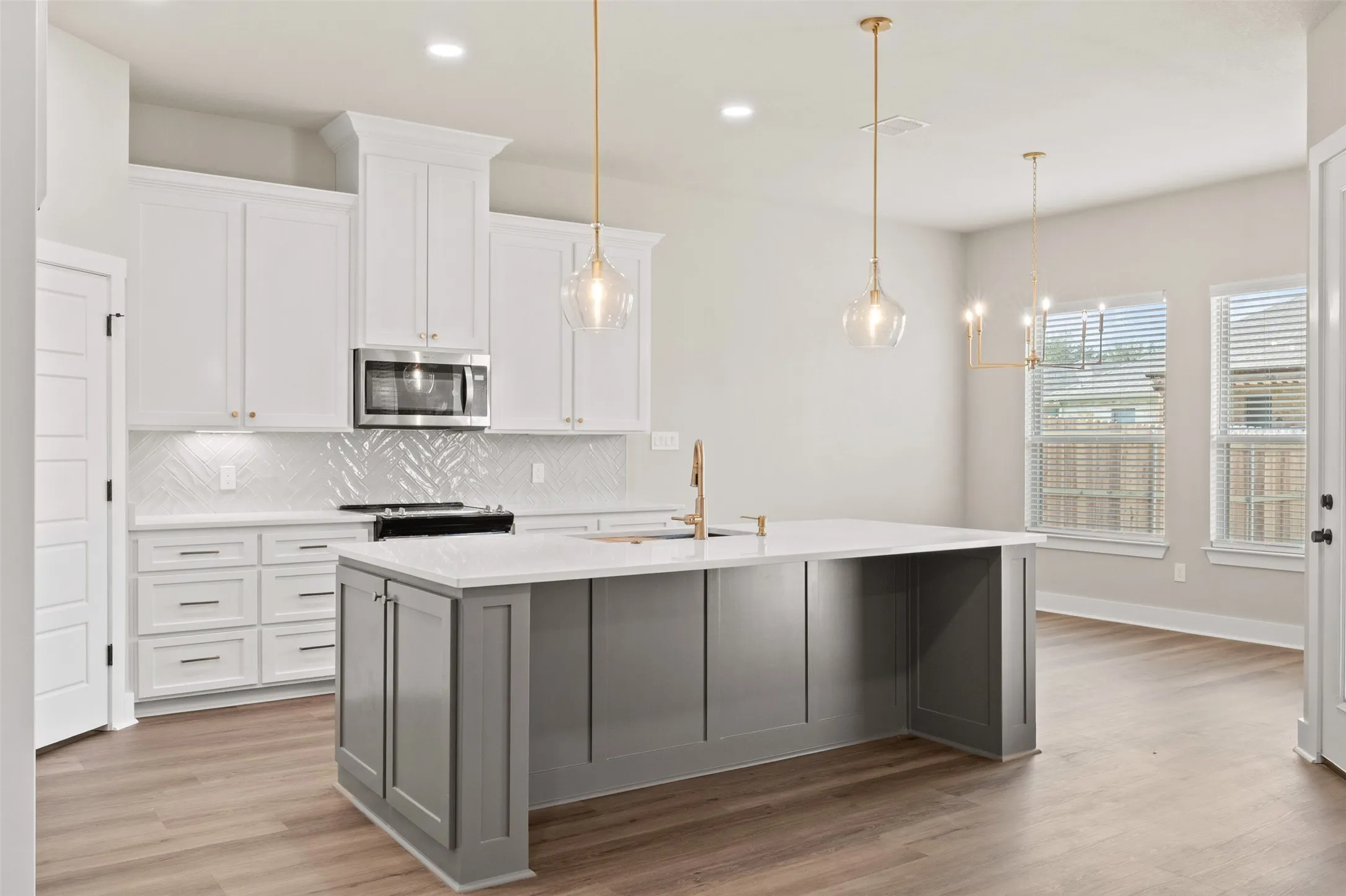 Modern kitchen featuring a large central island with a light-colored countertop, white shaker-style cabinetry, and wood-finish flooring
