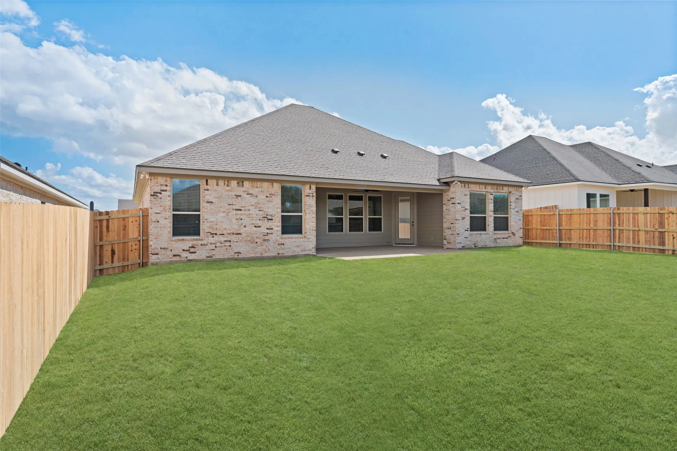 Expansive rear lawn featuring a privacy fence, brick exterior, multiple windows, and a covered patio area