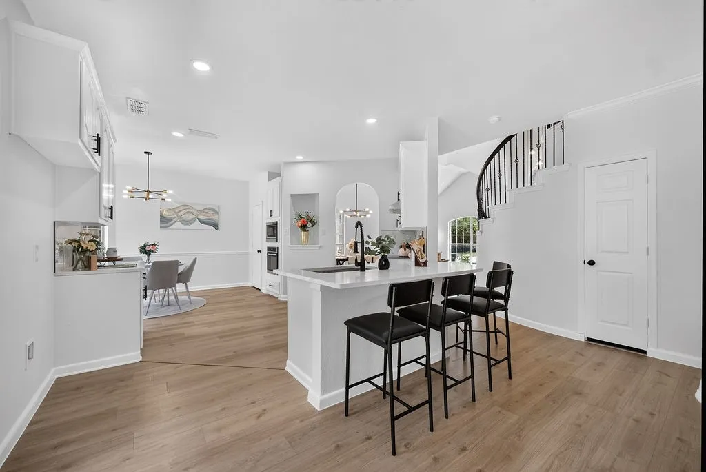 Open-concept interior featuring light wood-finish flooring, a kitchen island with a white countertop, recessed lighting, and a dining area with a contemporary chandelier