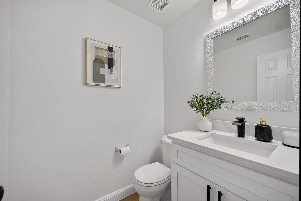 Powder room featuring a white single-sink vanity with a light-toned countertop, a black waterfall faucet, and a large framed mirror with integrated lighting