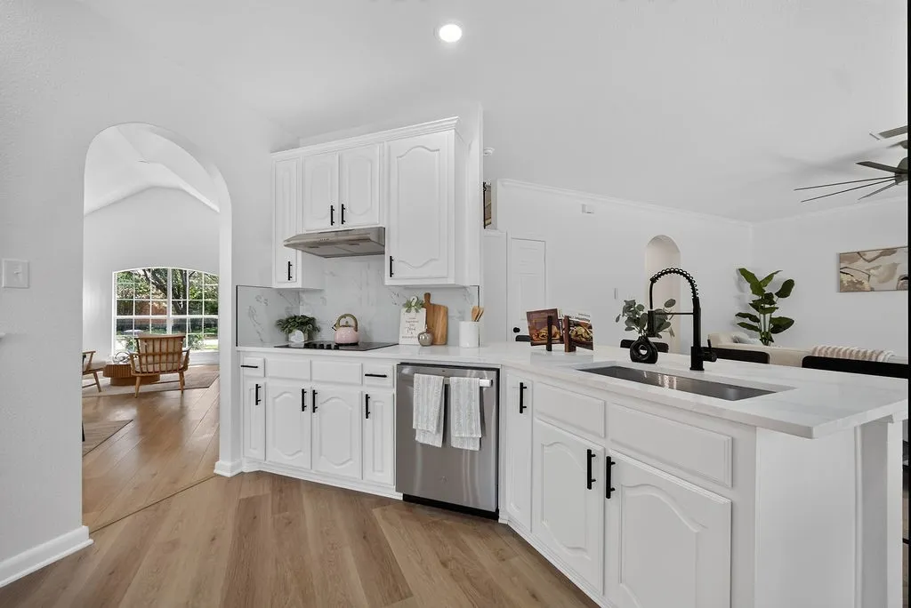 Modern kitchen featuring white cabinetry, light-toned countertops, a stainless steel dishwasher, and a black gooseneck faucet