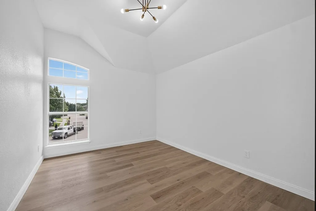 Vaulted ceiling room featuring a large arched window, wood-finish flooring, white walls, and a contemporary ceiling light fixture