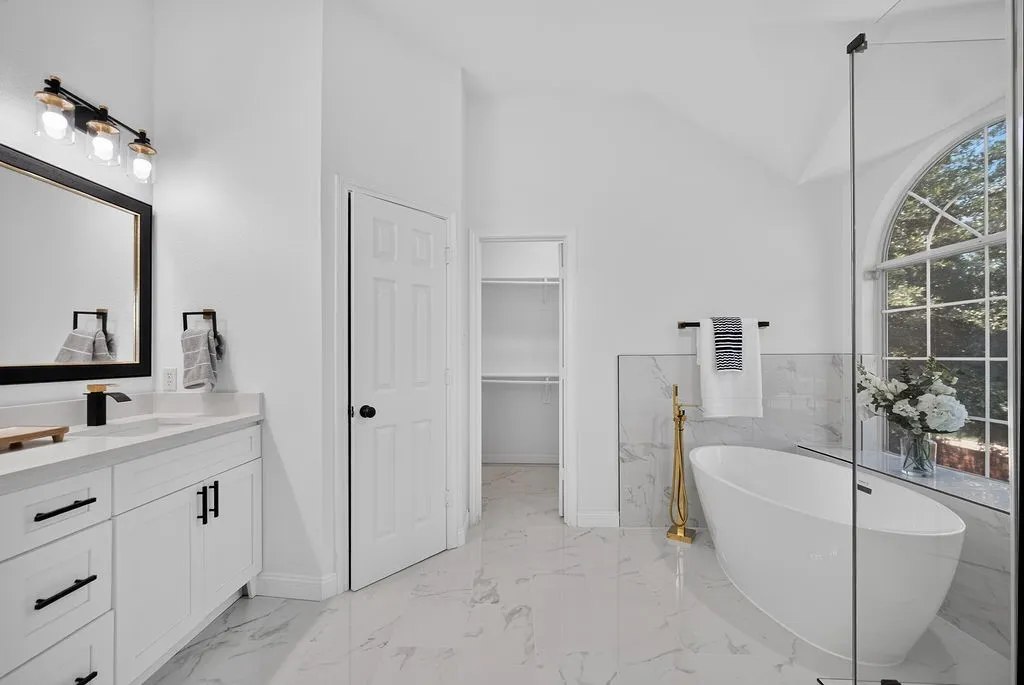 Bright bathroom with a freestanding soaking tub, a large arched window, and a glass-enclosed shower