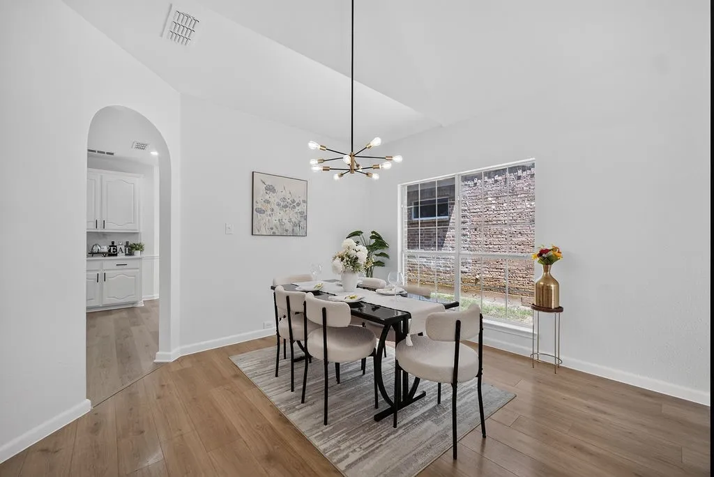 Spacious dining area featuring wood-finish flooring, a contemporary chandelier, vaulted ceilings, and a large window