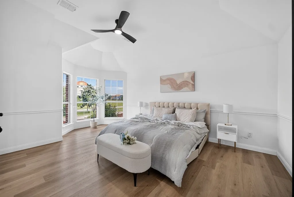 Spacious room featuring vaulted ceilings, bay windows, wood-finish flooring, wainscoting, and a modern ceiling fan