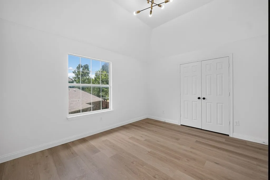 Vaulted ceiling room featuring light wood-finish flooring, a contemporary ceiling light fixture, a large window, and double bi-fold closet doors