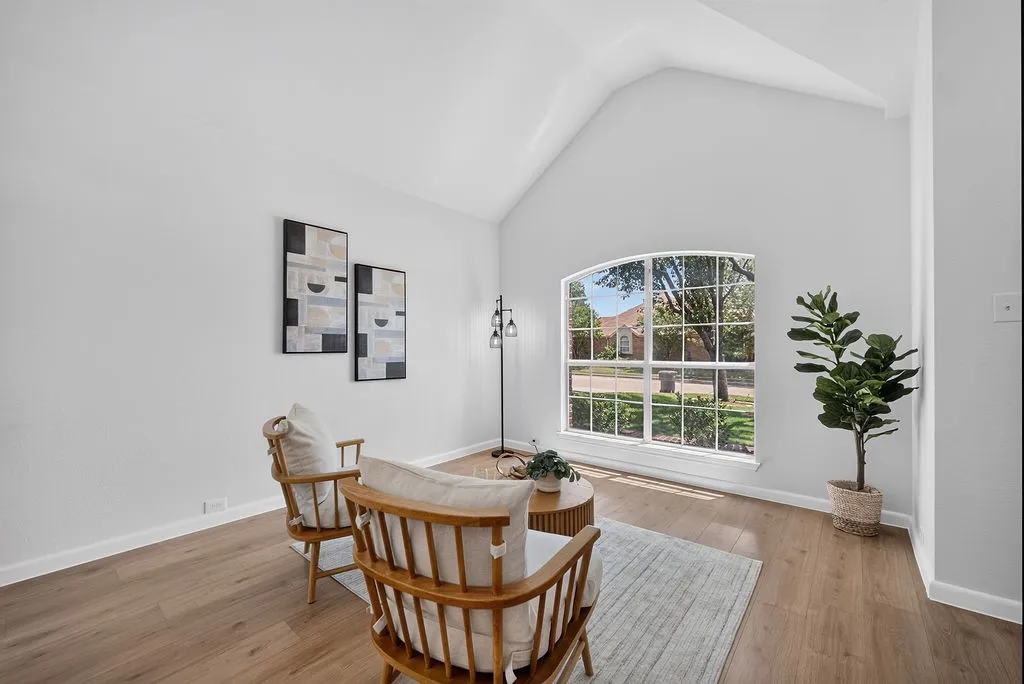 Vaulted ceiling living space featuring a large arched window, wood-finish flooring, and white baseboards