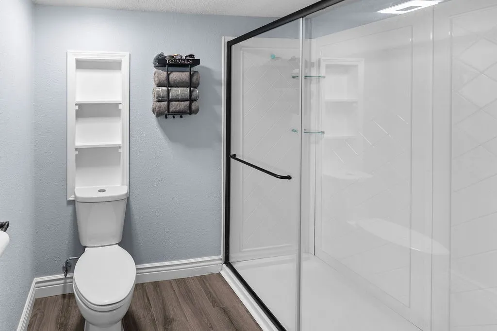 Primary ensuite bath has sparkling glass-door shower, LVP flooring, built-in shelving