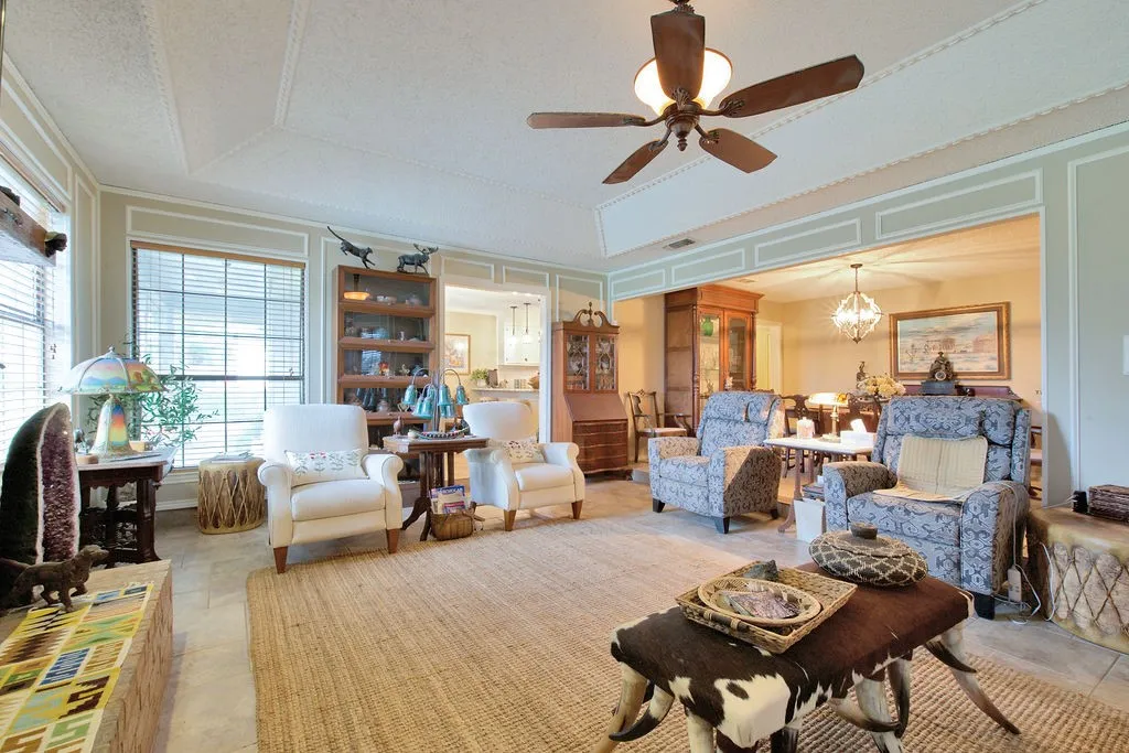Living area featuring tile flooring, a decorative ceiling with a ceiling fan, and large windows with blinds