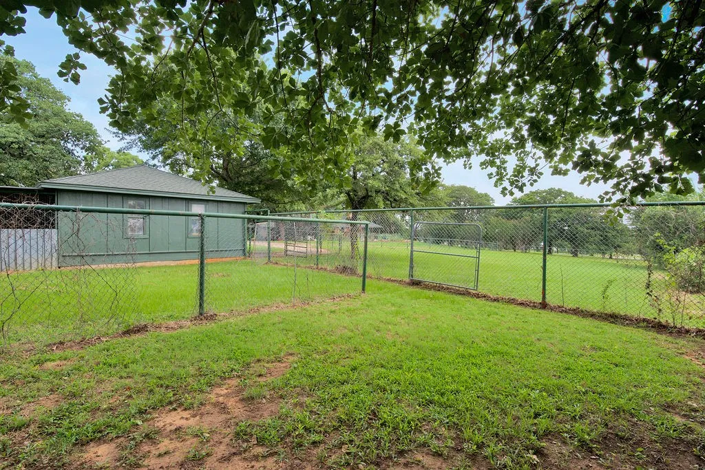 Expansive green space with mature trees and perimeter chain-link fencing.