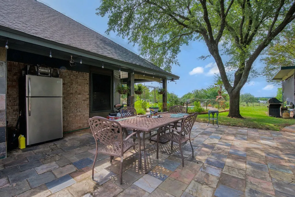 Outdoor patio featuring multi-toned paver flooring, a brick exterior wall, and a covered porch area with string lighting