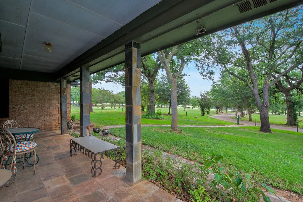 Covered patio featuring stone-look flooring, stone-clad support columns, and a brick exterior wall
