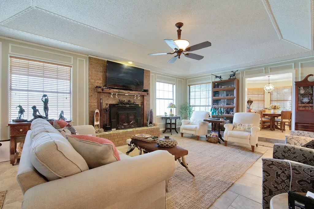 Spacious living area featuring a brick fireplace with a wood mantle, tray ceiling, and tile flooring