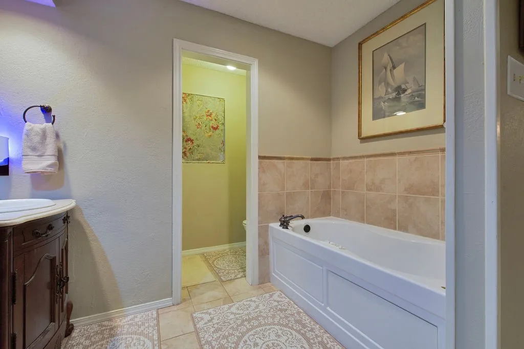 Bathroom featuring a large jetted tub with built-in tiled wainscoting, and tile flooring.