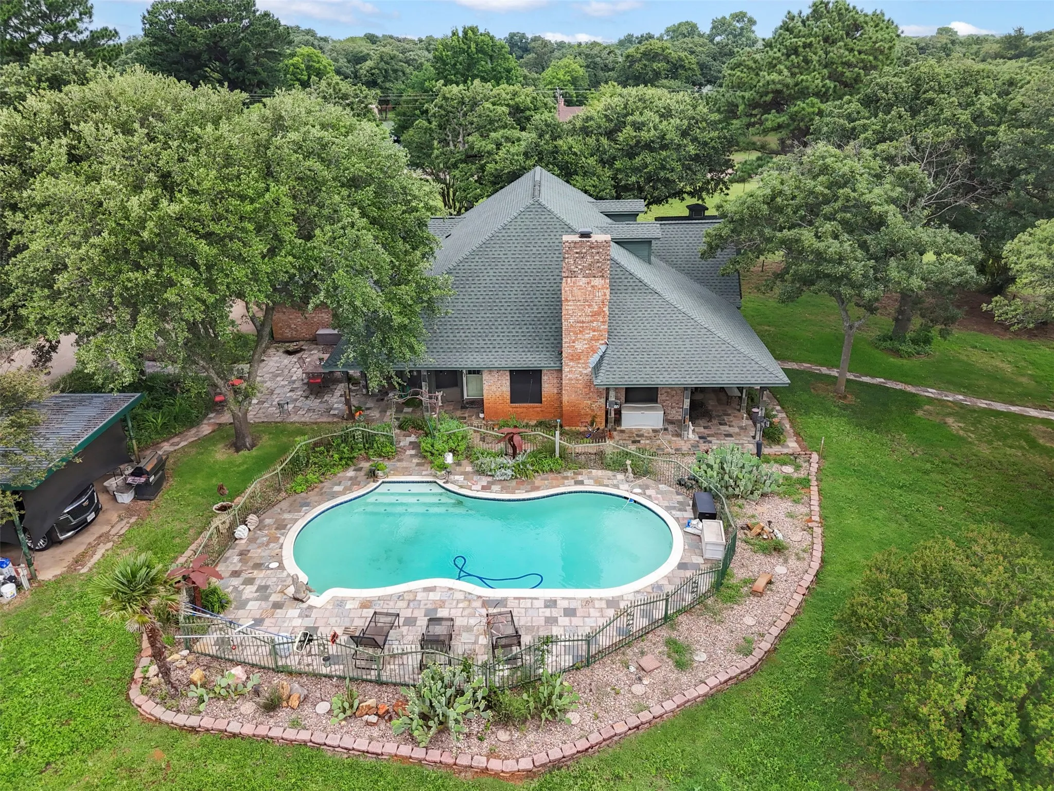 Expansive outdoor living area featuring a free-form swimming pool with a stone paver surround, a fenced perimeter, and established landscaping