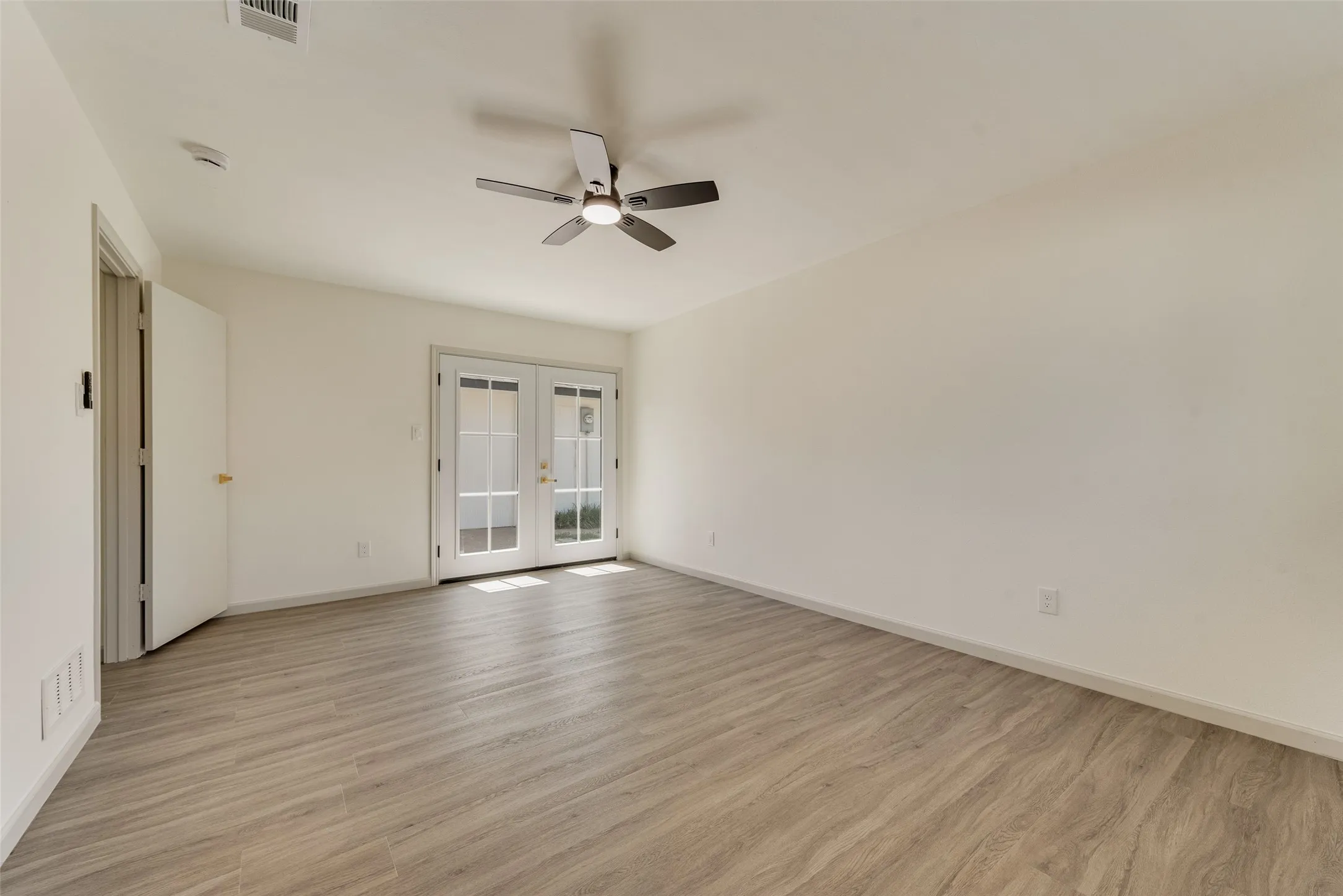 Spacious room featuring wood-finish flooring, white walls, and a ceiling fan with integrated lighting