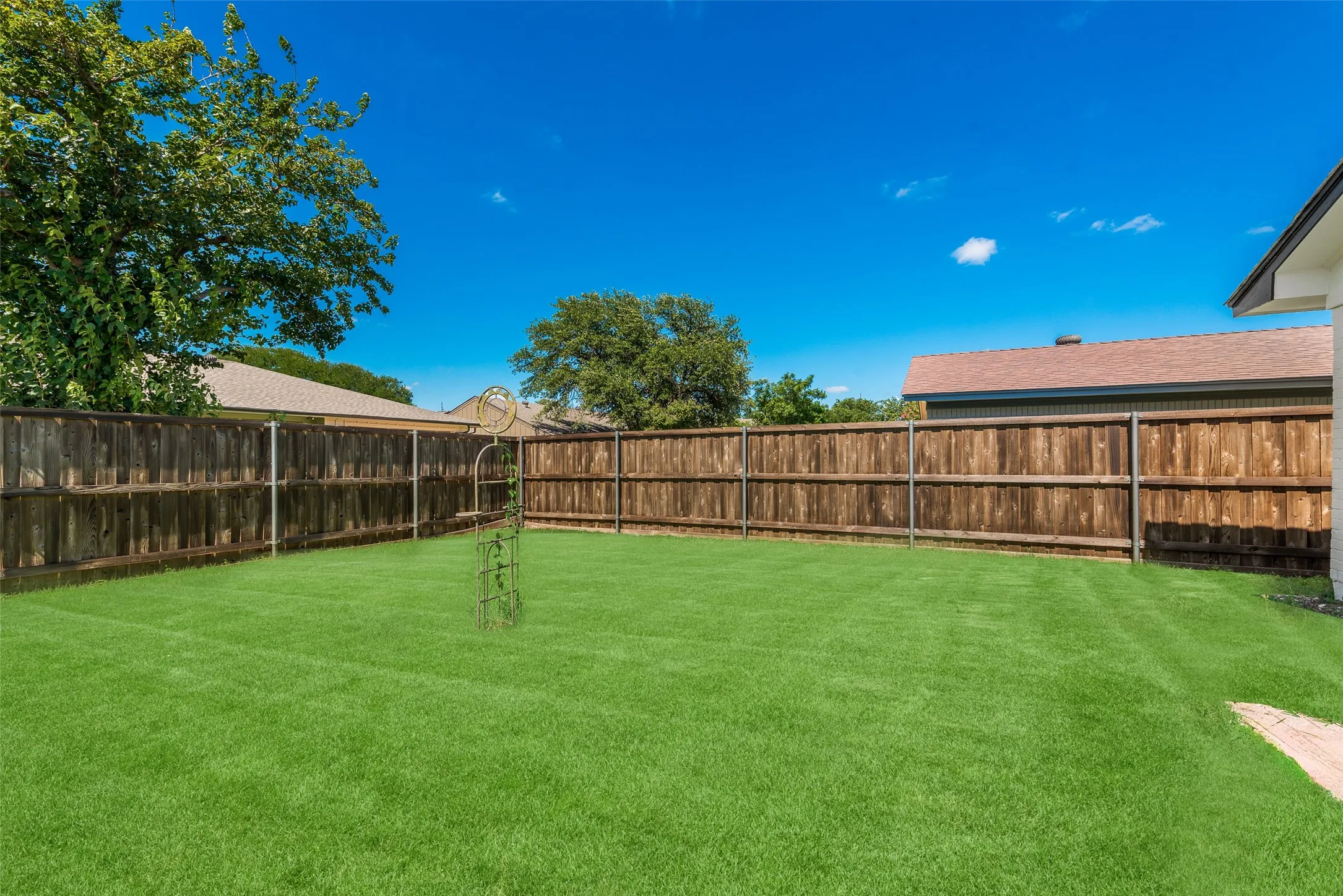 Expansive backyard featuring a lush green lawn, full wood privacy fencing, and mature perimeter trees