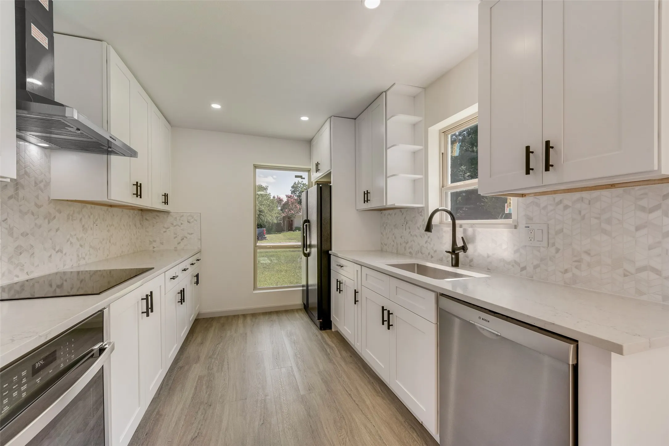 Contemporary kitchen featuring white shaker cabinetry, quartz countertops, a geometric tile backsplash, stainless steel appliances, and wood-finish flooring