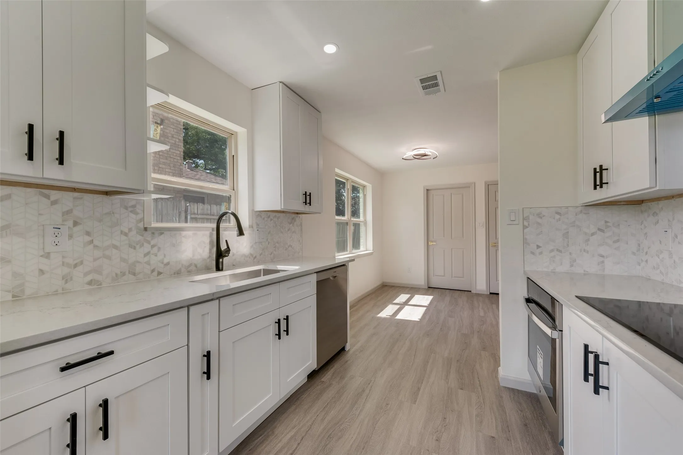 Modern kitchen featuring white shaker cabinetry, stainless steel sink with a black gooseneck faucet, light grey countertops, and a patterned backsplash