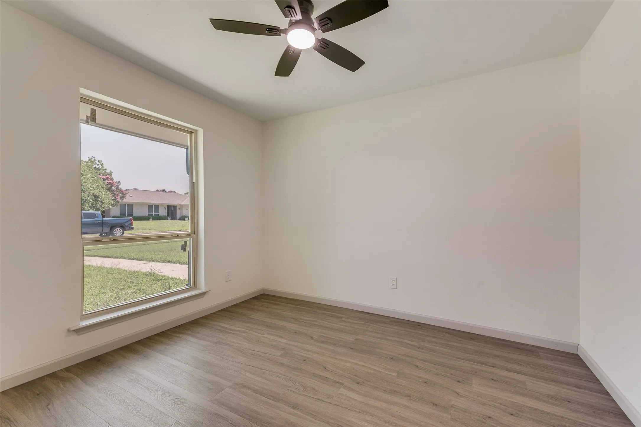 Room with wood-finish flooring, a large window, and a ceiling fan with integrated lighting