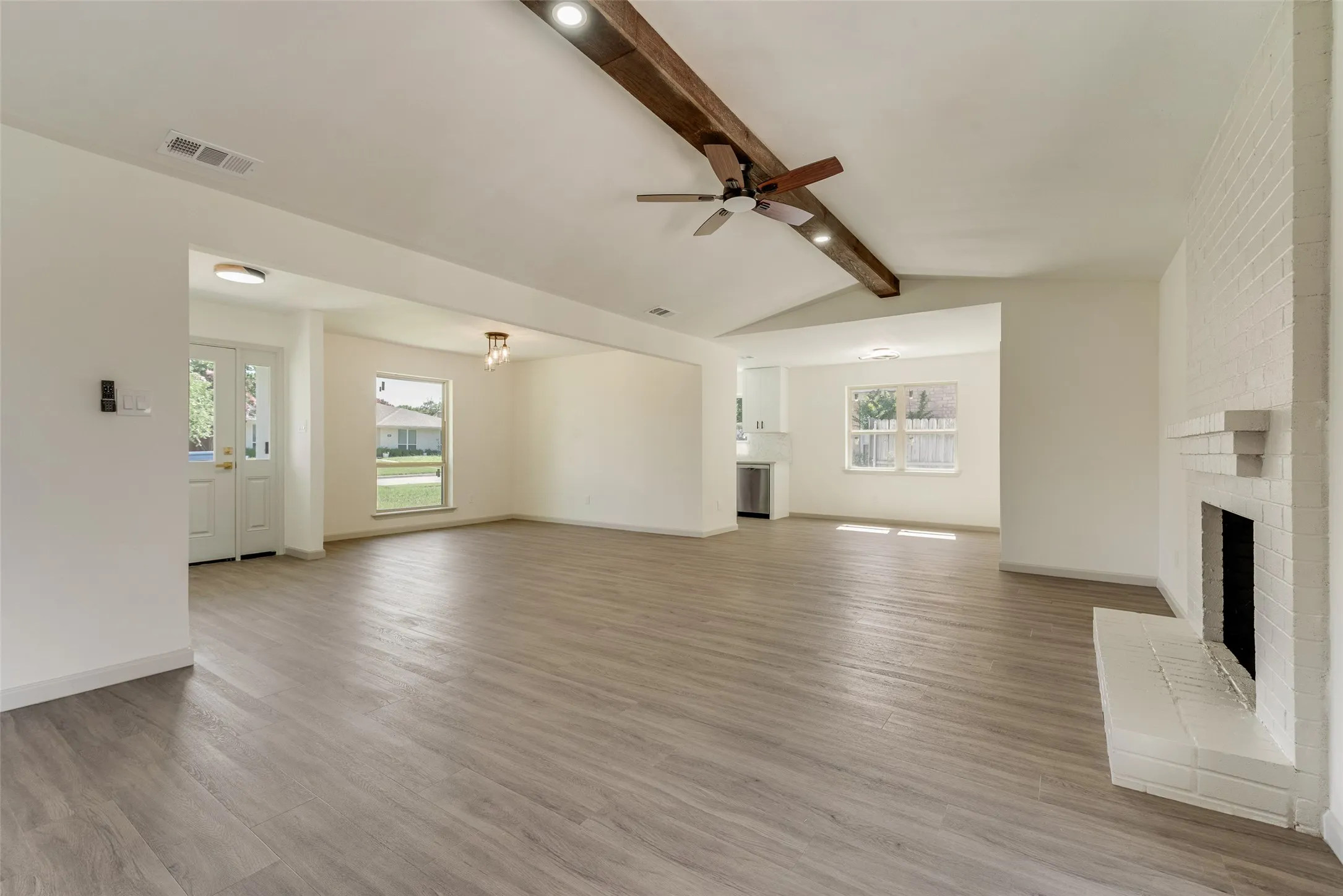 Spacious living area featuring wood-finish flooring, a white brick fireplace, and a vaulted ceiling with an exposed beam