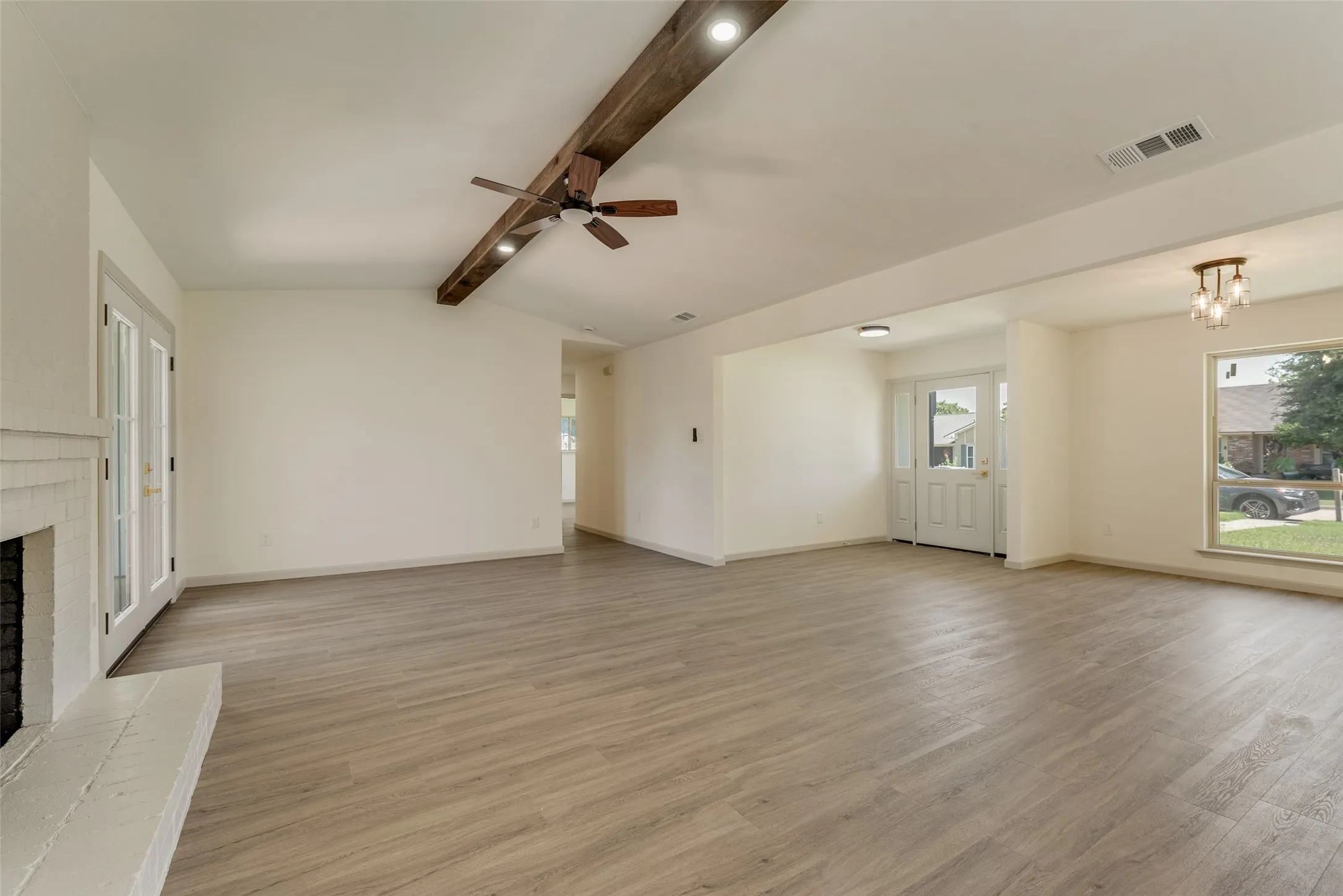 Spacious interior with wood-finish flooring, a painted brick fireplace, and double French doors