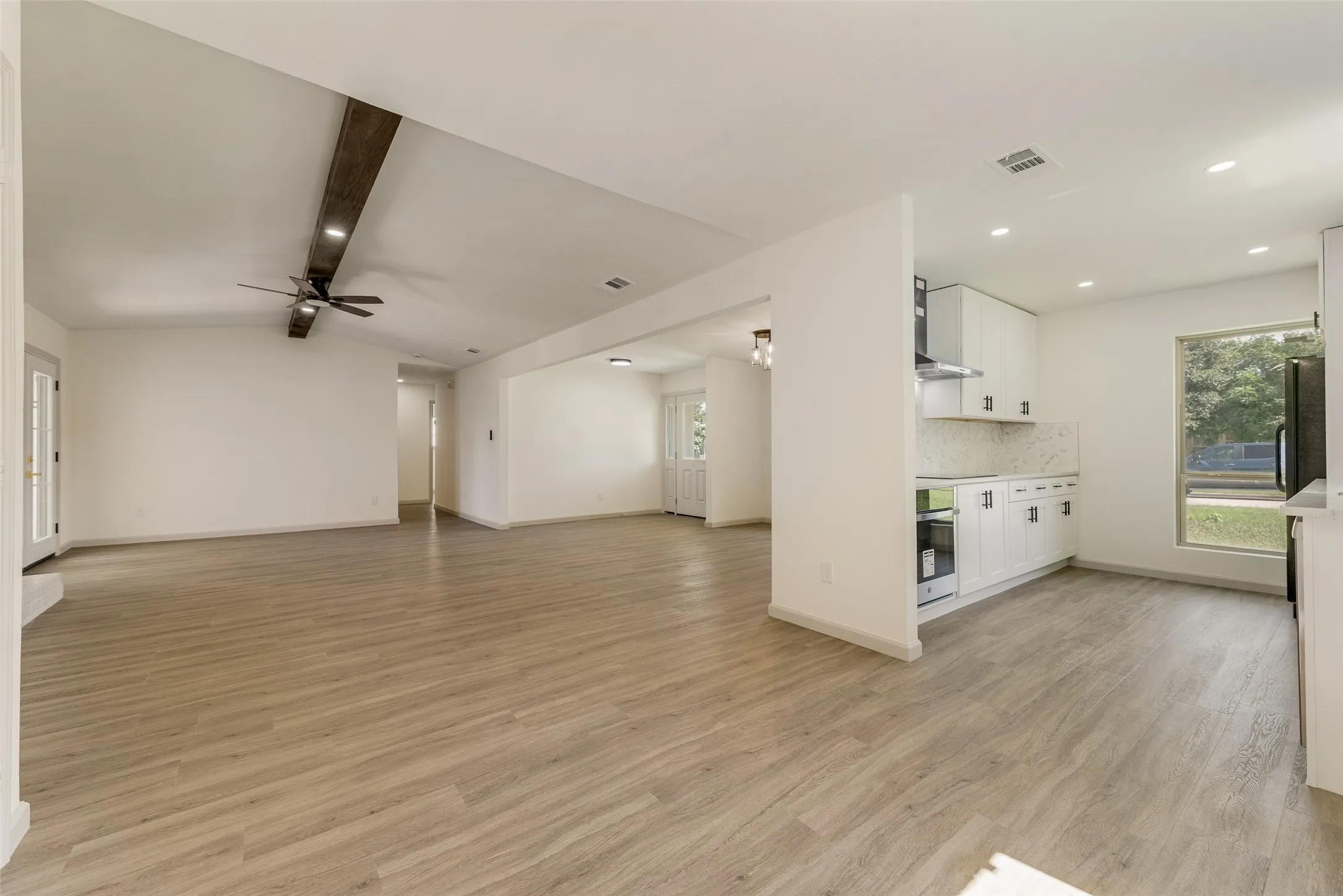 Expansive open-concept living area featuring wood-finish flooring, a vaulted ceiling with an exposed beam, and recessed lighting