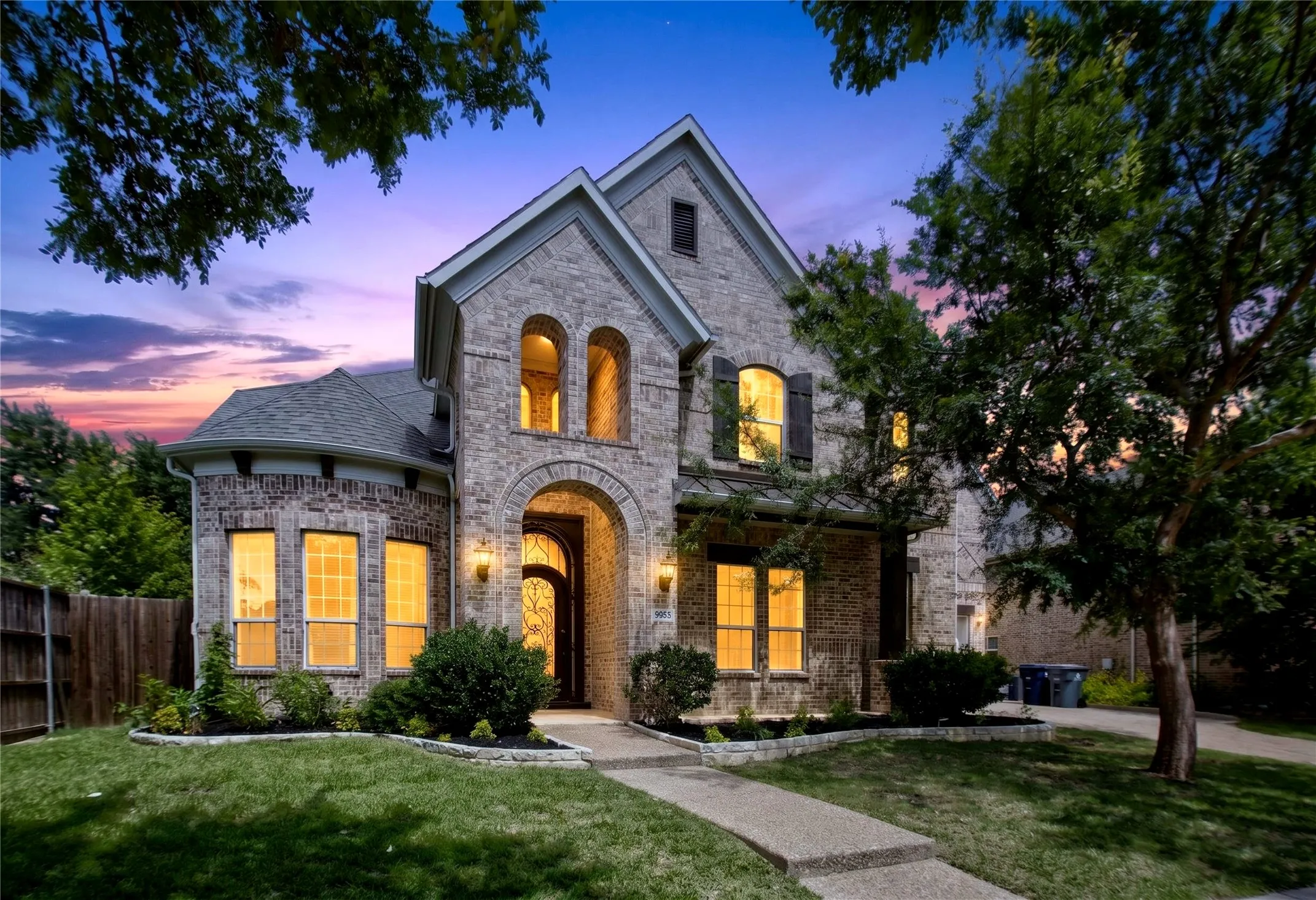 Stone and brick veneer exterior featuring a prominent arched entry, multiple gables, a gray shingle roof, and decorative window shutters